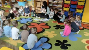 Dzieci siedzą z nauczycielką w kole i słuchają opowieści o kotach