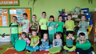 Dzieci w zielonych strojach uśmiechają się pozując do zdjęcia grupowego.