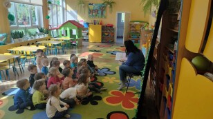 dzieci siedzą na dywanie, na krześle siedzi pani Sylwia, która czyta dzieciom bajkę