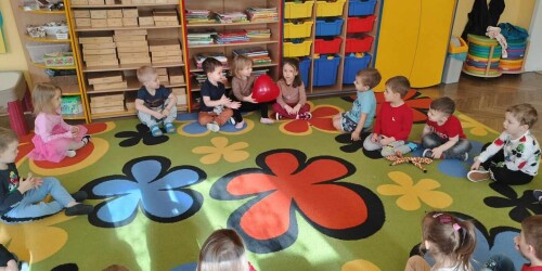 Dzieci siedzą na dywanie i uczestniczą w zabawie z czerwonym balonem