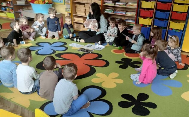 Dzieci siedzą z nauczycielką w kole i słuchają opowieści o kotach