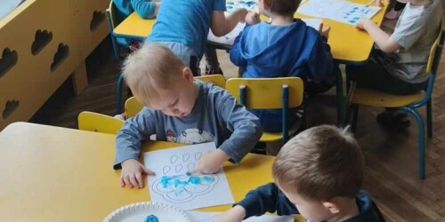 Dzieci siedzą przy stoliku i malują farbami chmurkę
