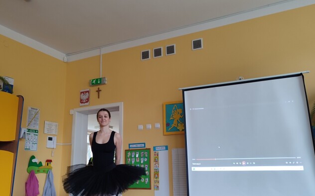 Baletnica stoi na środku sali prezentując swój czarny baletowy strój