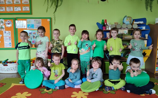 Dzieci w zielonych strojach uśmiechają się pozując do zdjęcia grupowego.