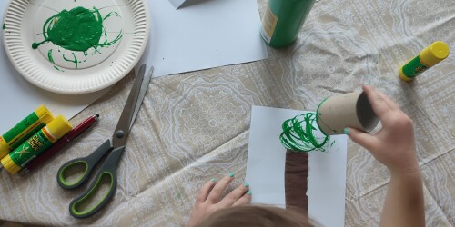 dzieci stemplują rolką po papierze maczając ją w zielonej farbie