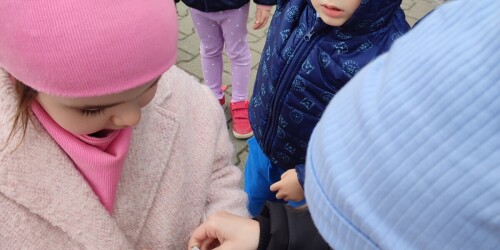 Dziewczynka trzyma w dłoniach widokówkę, stojący obok niej chłopiec przykleja znaczek pocztowy.