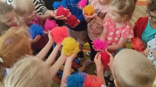 Dzieci stoją w kręgu i trzymają w dłoniach zwinięte chusty z kolorowej organzy.