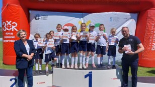 Przedszkolaki stoją na podium z numerem 1 w strojach sportowych.